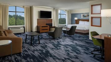 A hotel room with a bed, a TV, a desk, a chair, a sofa, and a view of the outdoors.