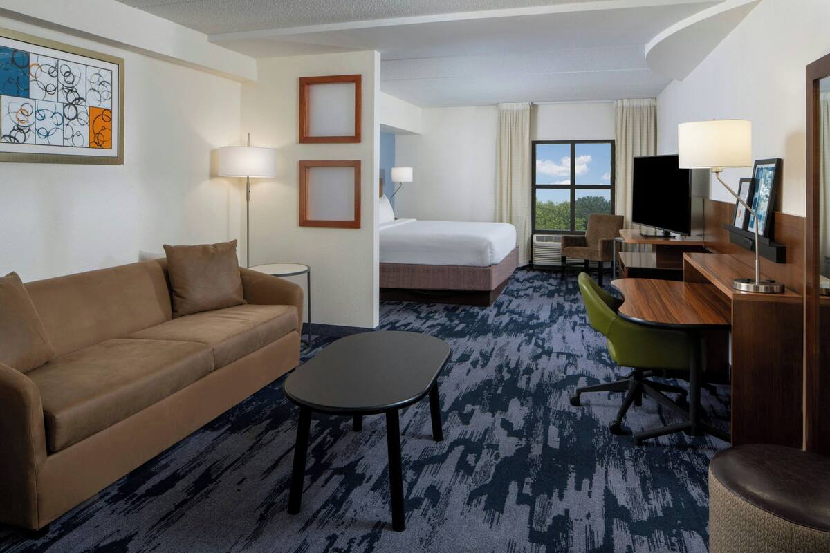 A hotel room with a bed, a sofa, a desk, a TV, and a window with a view.
