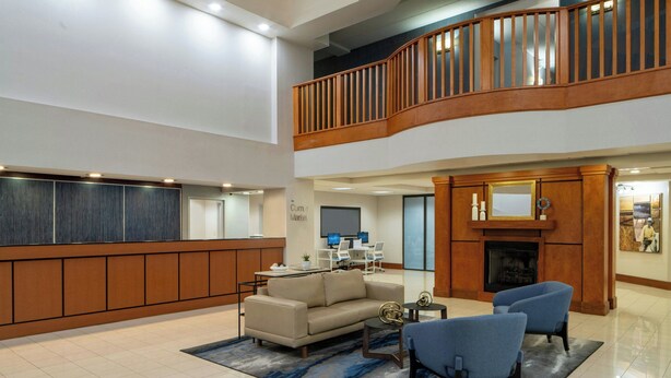A spacious lobby with a high ceiling, a wooden staircase, a fireplace, and a seating area with a coffee table and chairs. - Fairfield Inn & Suites Atlanta Airport South/Sullivan Road (College Park)