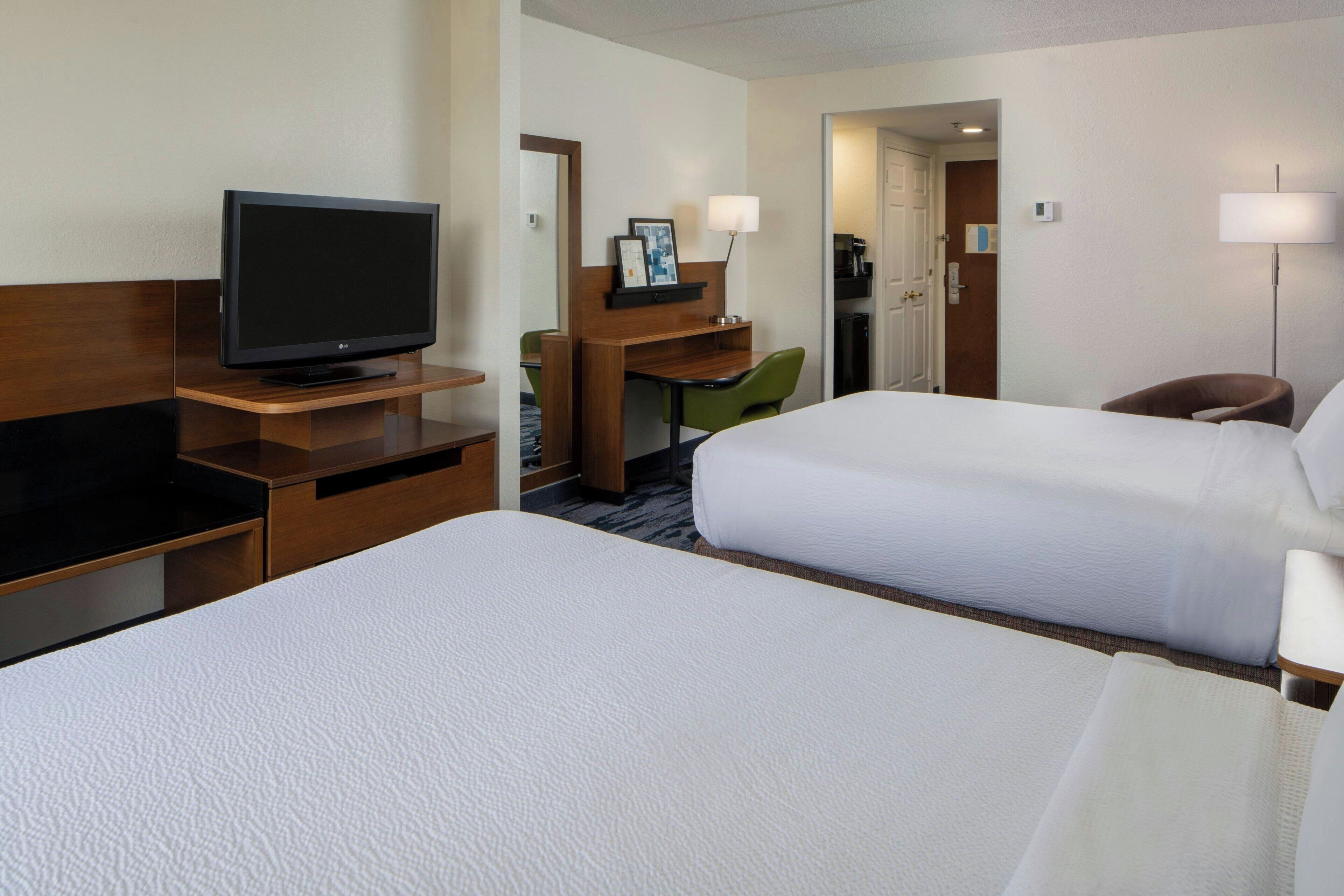 Una habitación de hotel con dos camas, un escritorio con televisor, una silla y una lámpara.