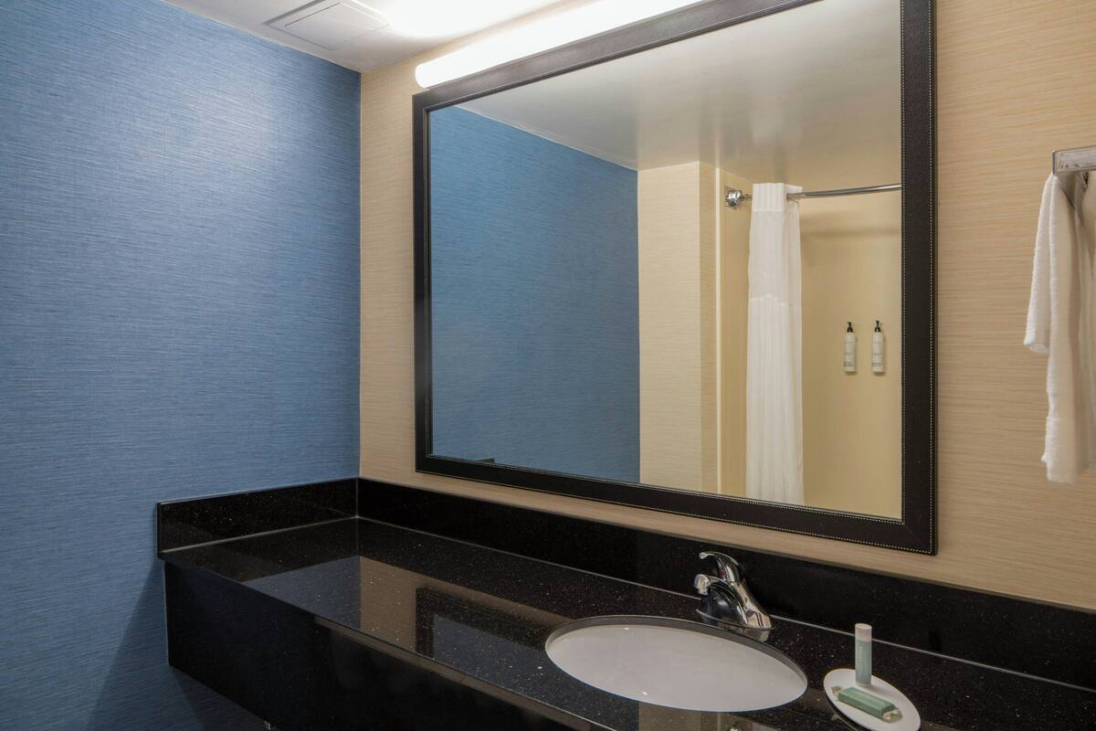A modern bathroom with a large mirror, black countertop, and a white sink.