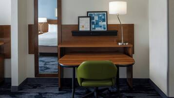 A hotel room with a bed, a desk with a chair, a lamp, and framed artwork on the wall.