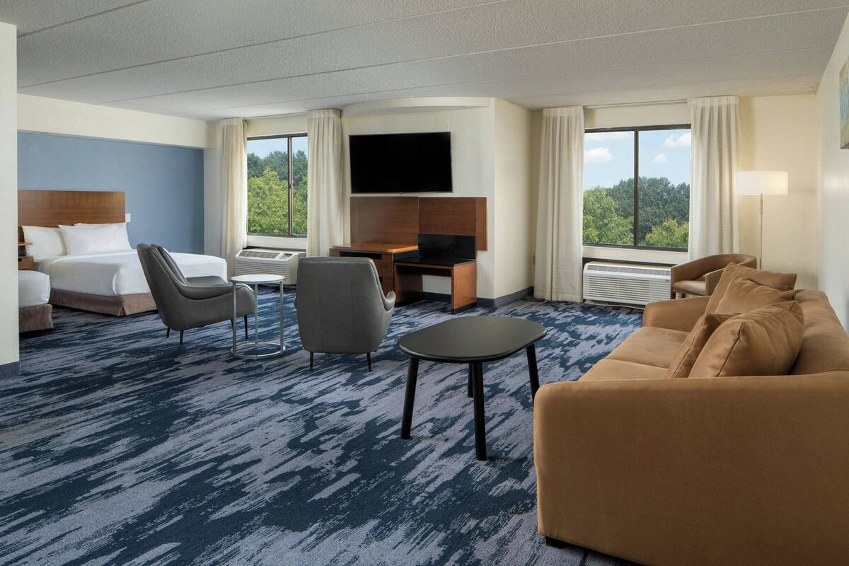A hotel room with a bed, two chairs, a desk, a TV, and a sofa.