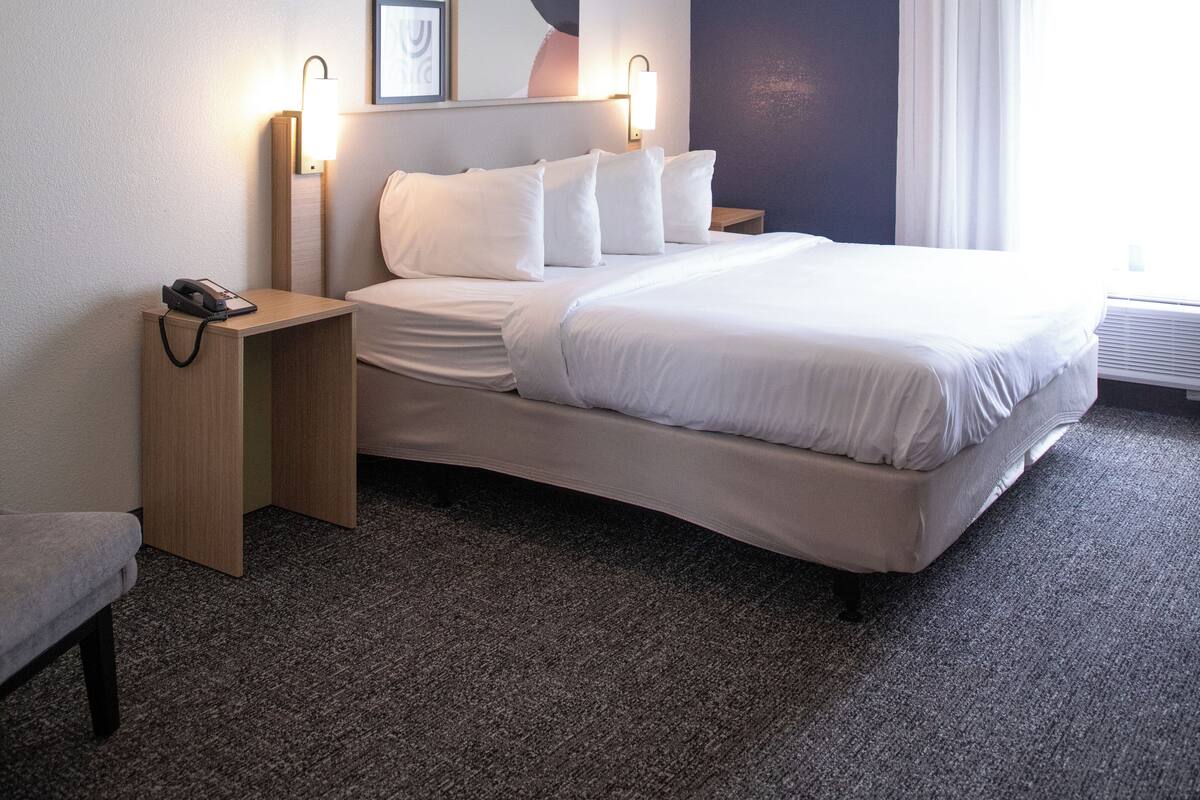 A hotel room with a large bed, two bedside tables, a nightstand, a framed picture, and a window with curtains.