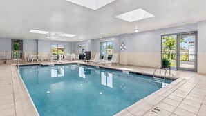 Una piscina interior con agua cristalina, sillas de descanso blancas y tragaluces.