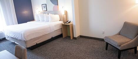 Una habitación de hotel con cama, mesita de noche, silla y una pequeña mesa.