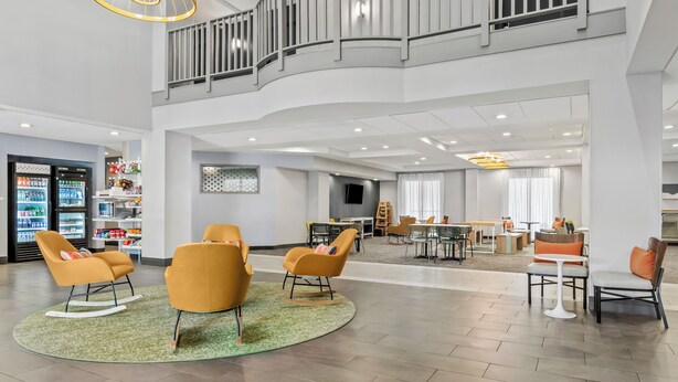 Un vestíbulo amplio con mobiliario moderno, una zona de estar central y una escalera que conduce a un nivel superior.