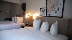 Habitación de hotel con dos camas, una mesita de noche con lámpara, teléfono y una obra de arte en la pared.