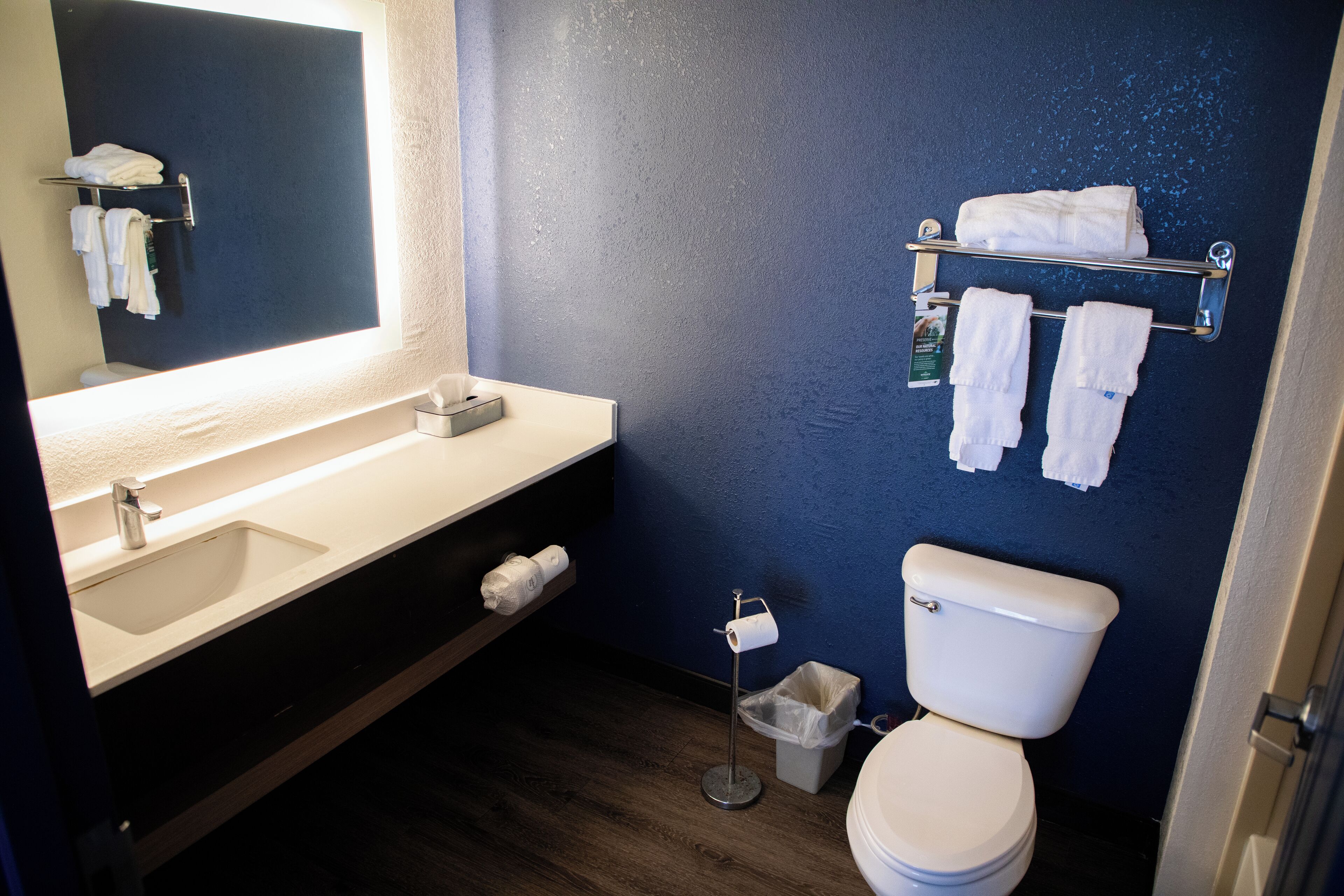 A bathroom with a sink, mirror, towel rack, toilet, and a trash bin.