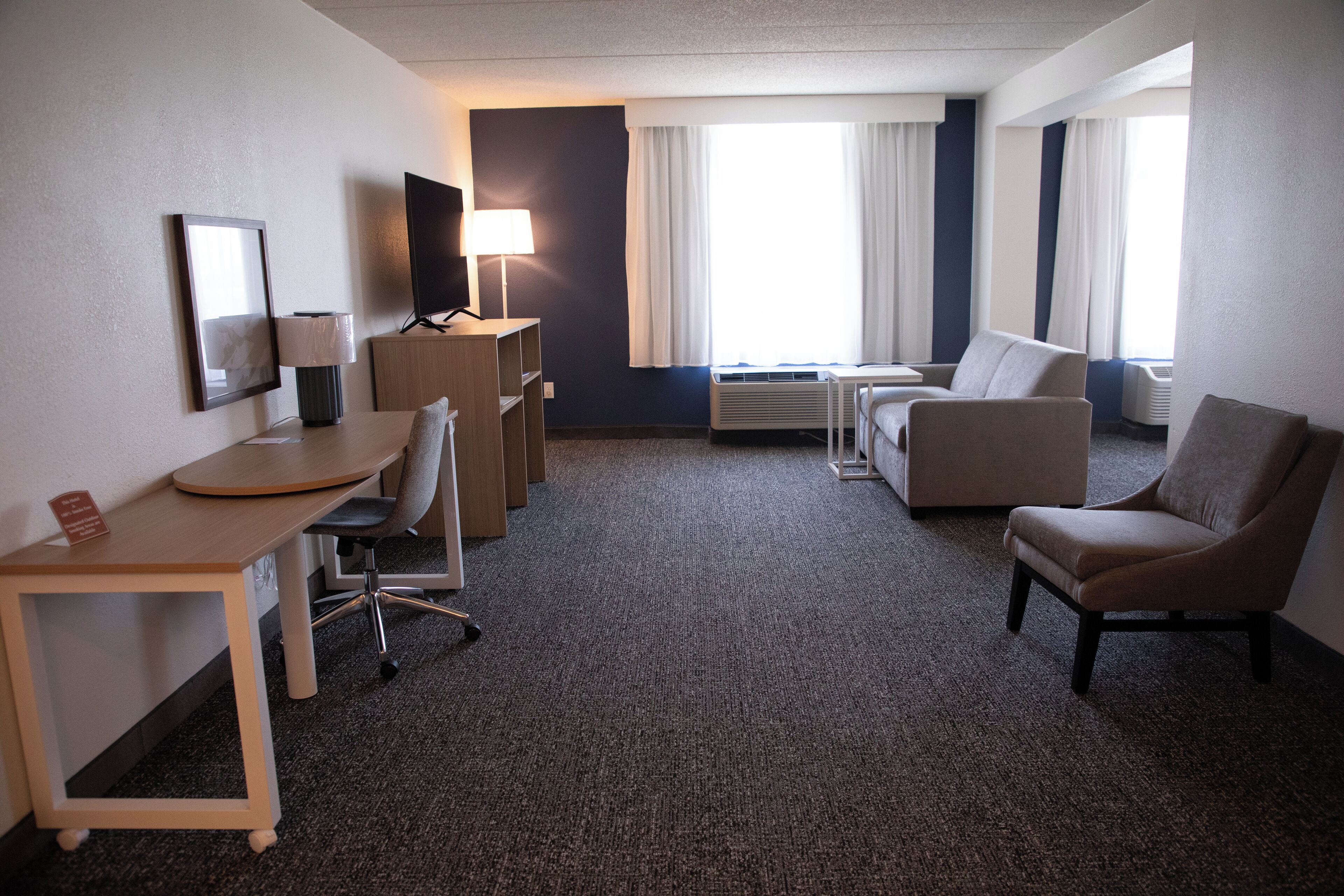 Une chambre d’hôtel équipée d’un bureau, de deux fauteuils, d’un canapé, d’une télévision, d’une lampe et d’une fenêtre avec des rideaux.