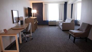 Une chambre d’hôtel équipée d’un bureau, de deux fauteuils, d’un canapé, d’une télévision, d’une lampe et d’une fenêtre avec des rideaux.