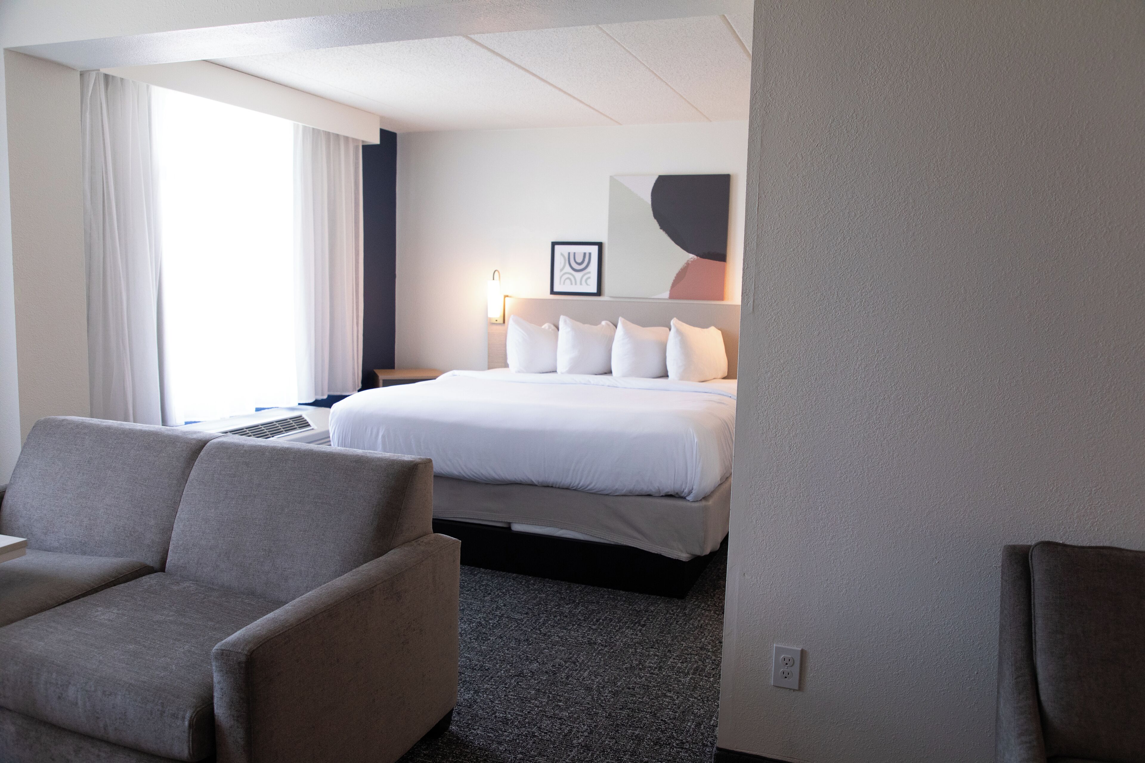 Ein Hotelzimmer mit Bett, Sofa, Schreibtisch und einem fenster mit Vorhängen.