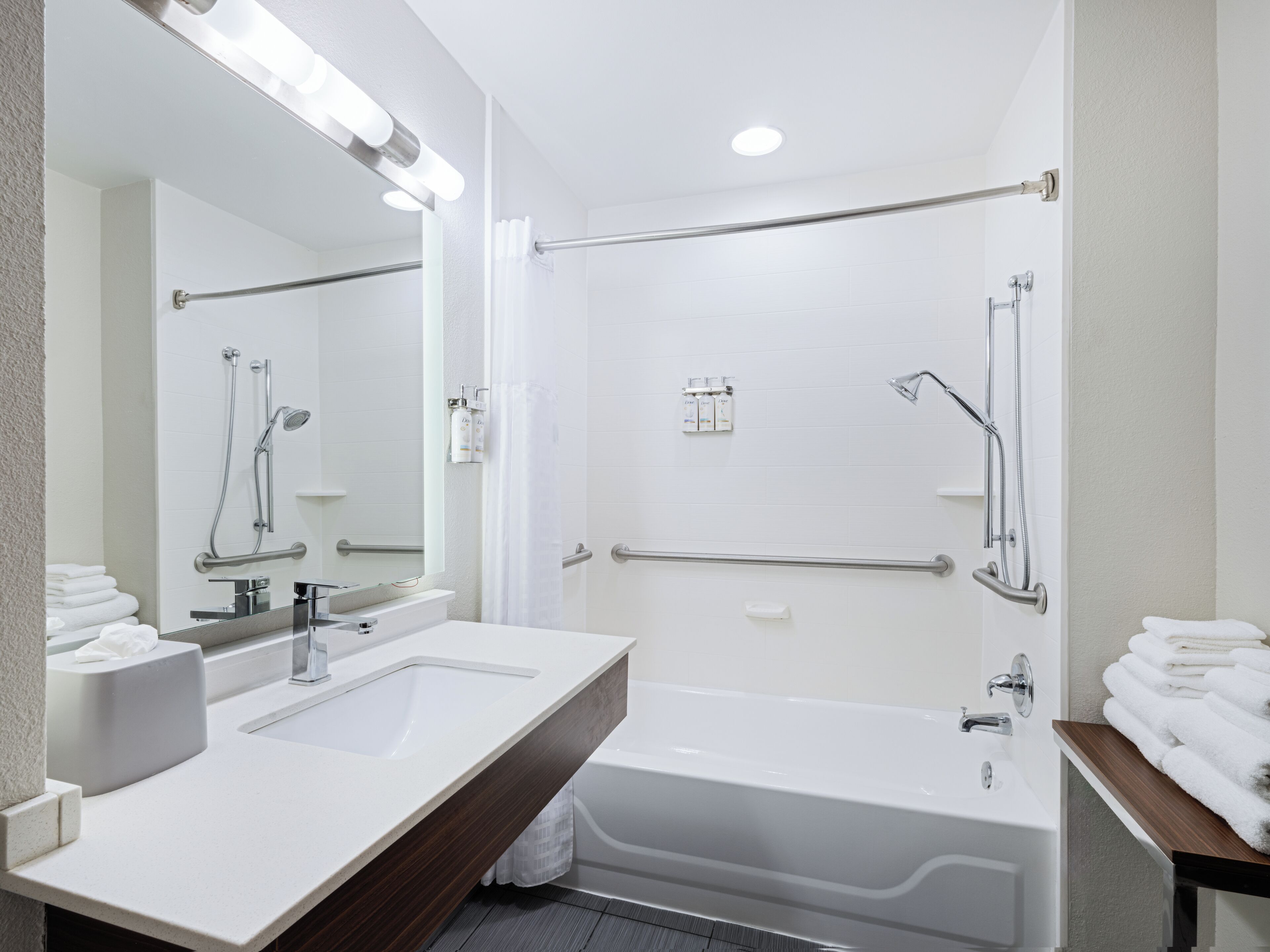 A modern bathroom with a large mirror, dual sinks, a bathtub, and a shower area.