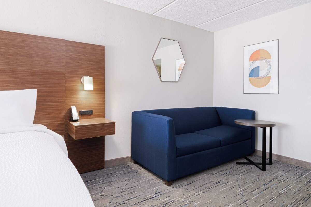Une chambre d’hôtel avec un lit, une tête de lit en bois, un canapé bleu, une petite table et un miroir fixé au mur.