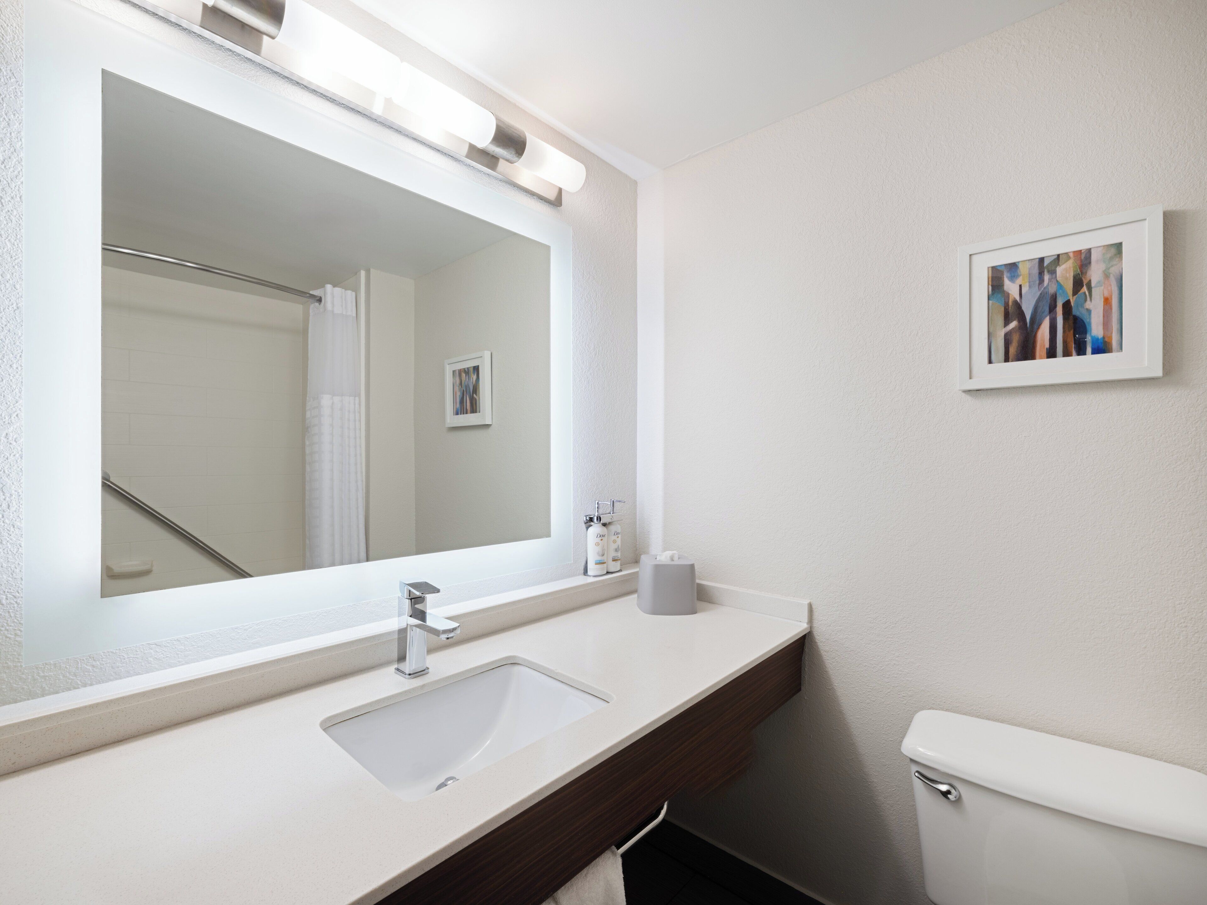 A bathroom with a large mirror, a sink, a toilet, and a framed abstract painting on the wall.