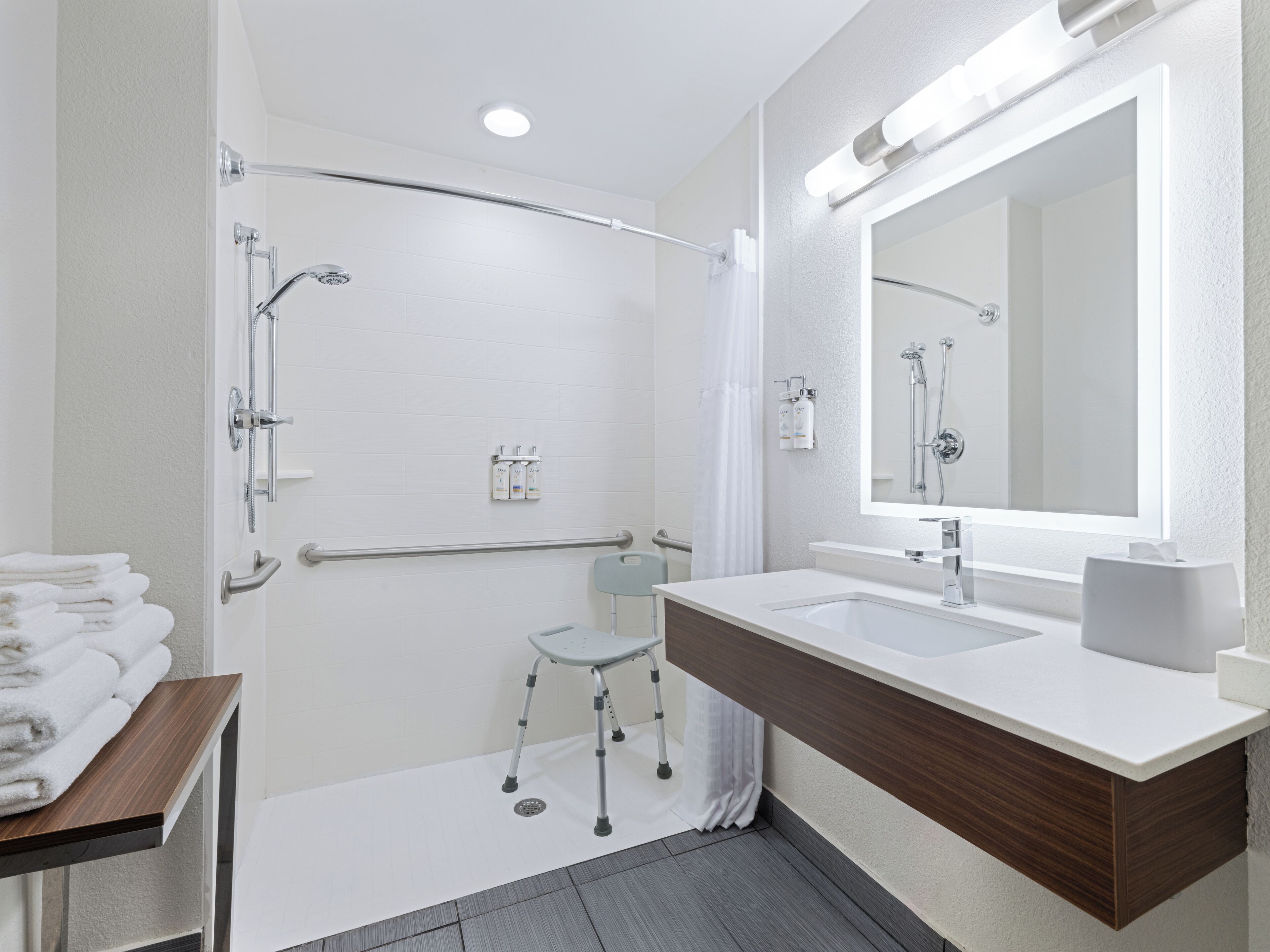 A modern bathroom with a shower, a vanity with a mirror, and a small stool.