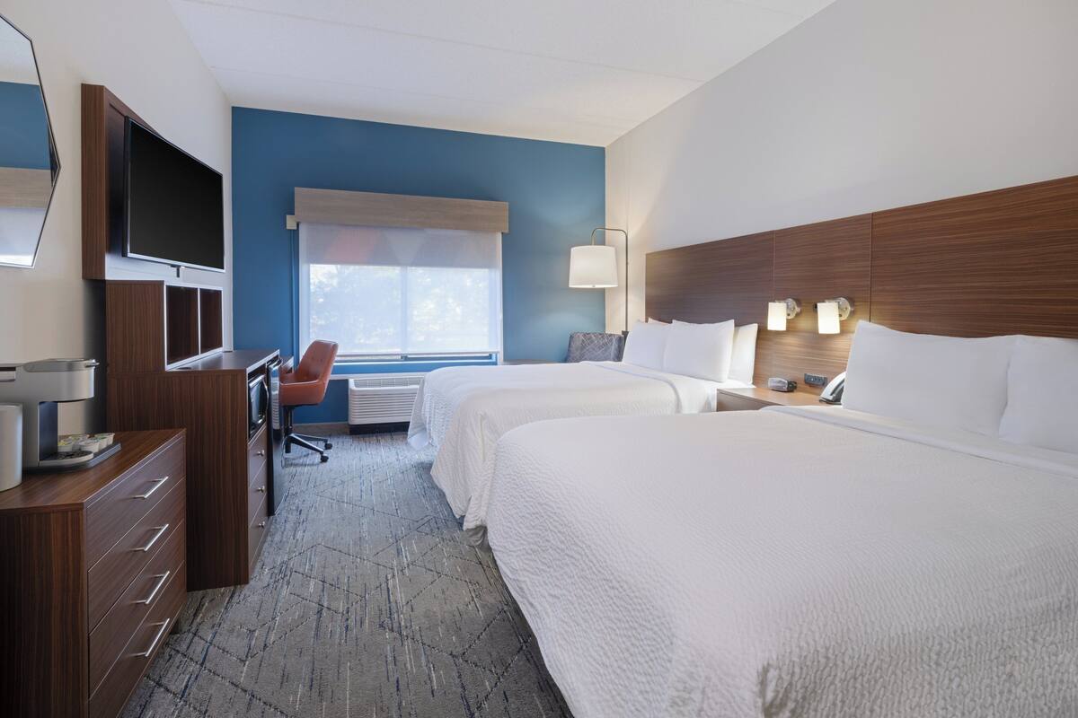 A hotel room with two beds, a desk, a chair, a TV, and a window with blinds.