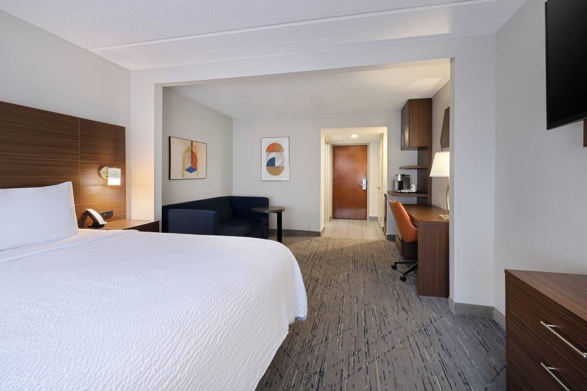 A hotel room with a large bed, a desk, a chair, and a TV on the wall.