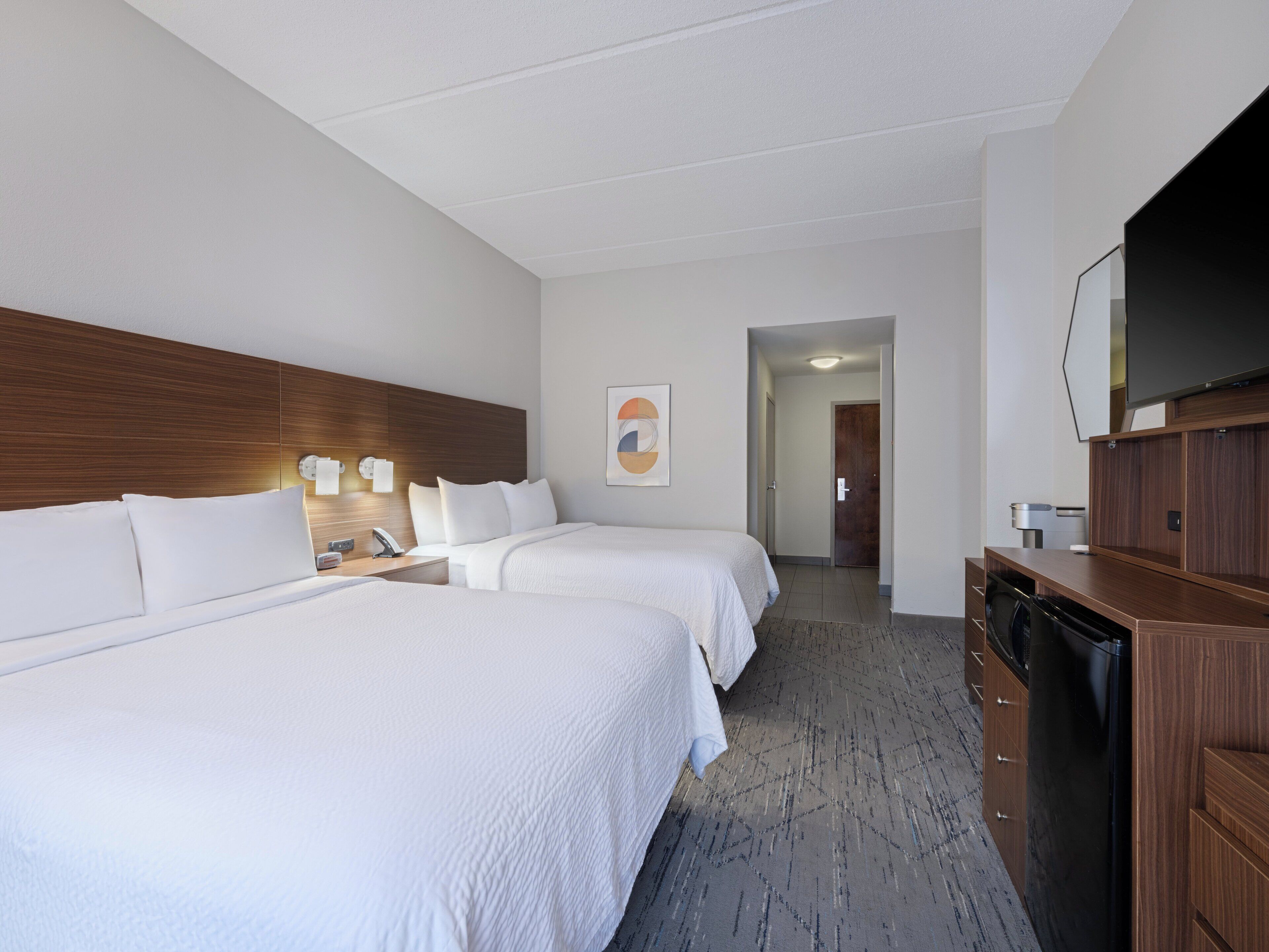 A hotel room with two beds, a wooden headboard, a flat-screen TV, and a minibar.