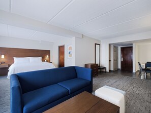 Une chambre d’hôtel avec un lit, un canapé bleu, une table basse en bois, une commode et un bureau avec des chaises.
