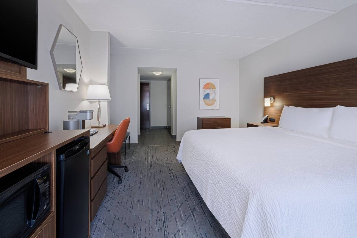 A hotel room with a bed, desk, chair, and a TV.