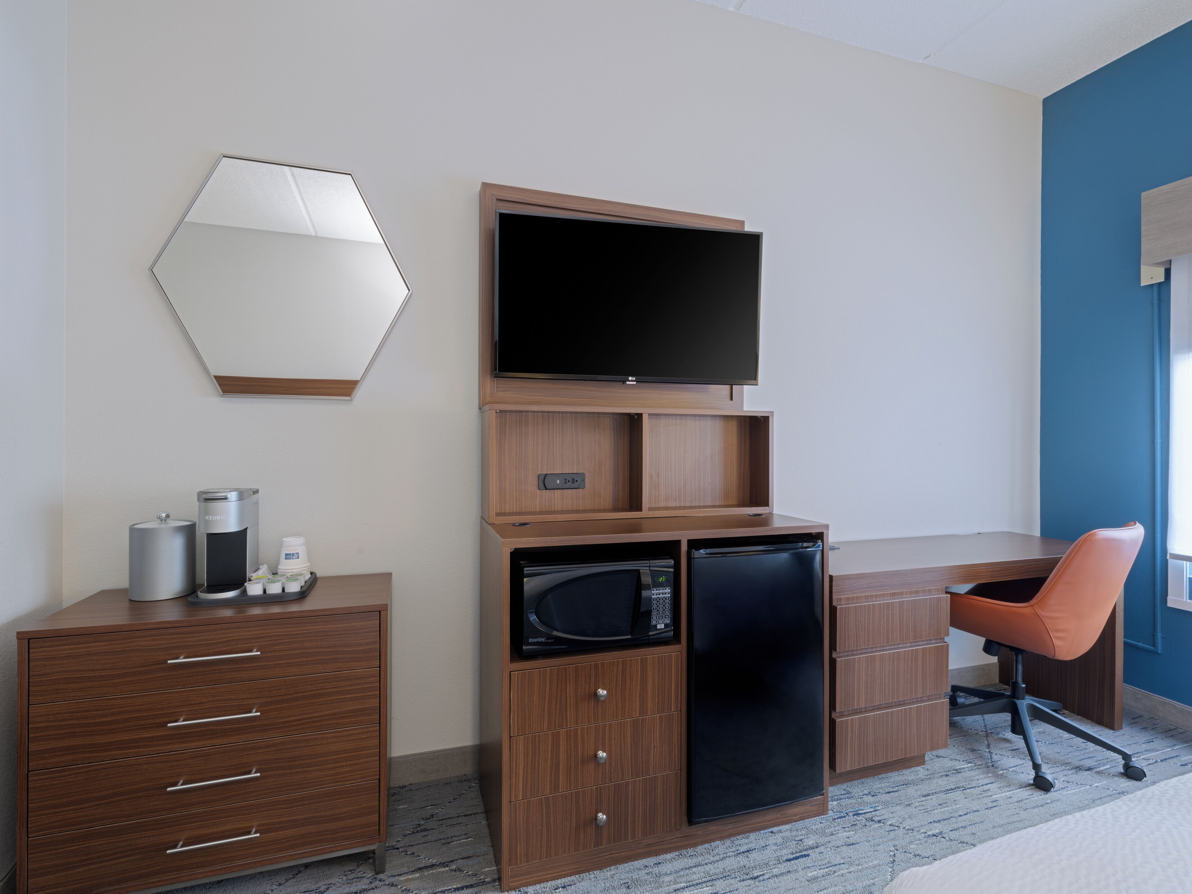 Une chambre d’hôtel avec un bureau en bois, un téléviseur à écran plat, un four à micro-ondes, une machine à café et une chaise orange.