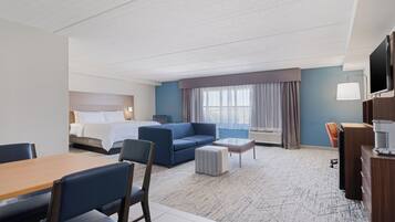 A hotel room with a bed, a blue sofa, a dining table with chairs, a small coffee table, and a TV.