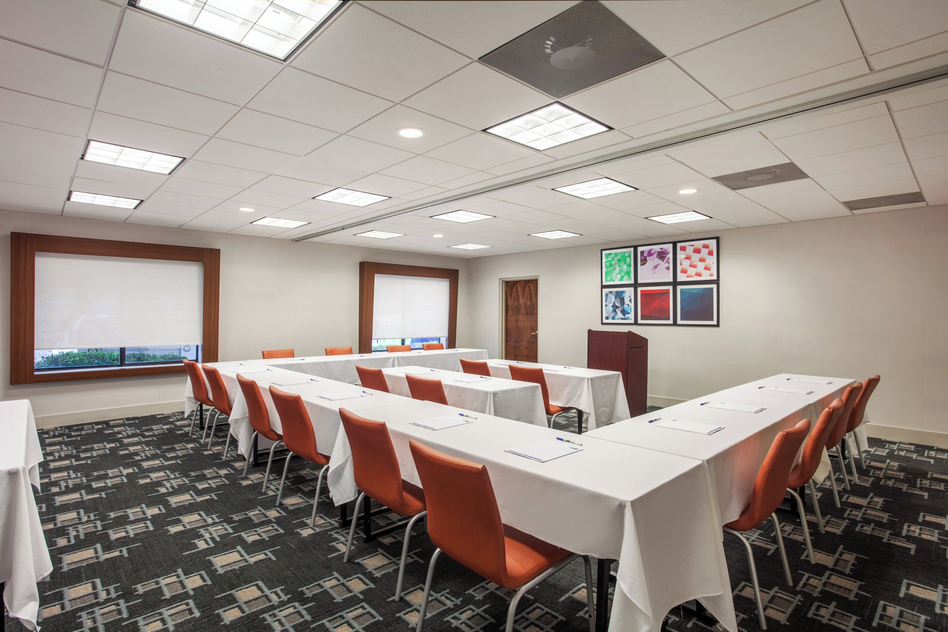 A conference room with multiple tables and chairs, large windows, and a patterned carpet.