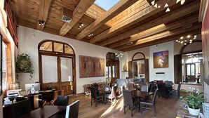 A spacious dining area with wooden beams, large windows, and a mix of seating arrangements. - The Inn at Vanessie (Santa Fe)