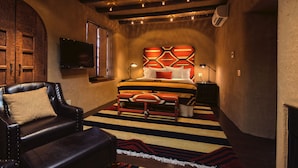 A cozy bedroom with a bed, a leather chair, and a television on the wall. - The Inn at Vanessie (Santa Fe)