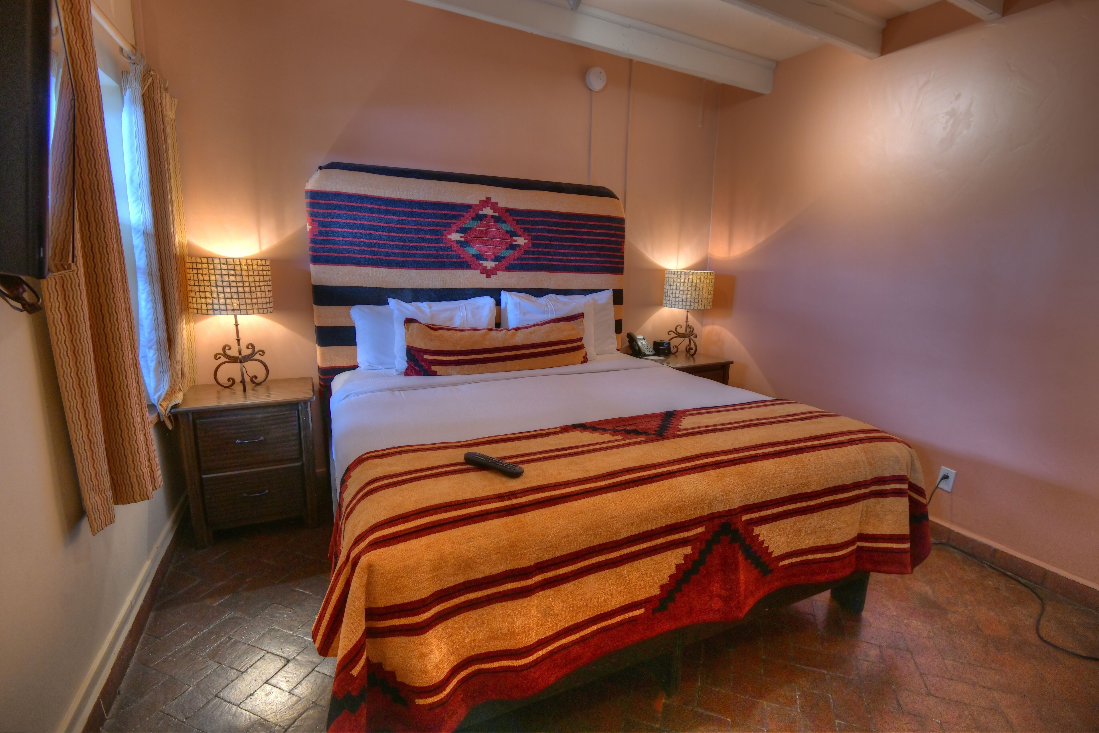 A neatly made bed with a striped blanket, a headboard with a decorative pattern, two bedside lamps, and a nightstand with a telephone.