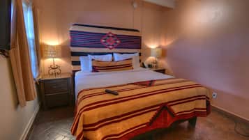 A neatly made bed with a striped blanket, a headboard with a decorative pattern, two bedside lamps, and a nightstand with a telephone.