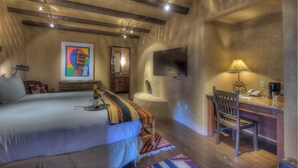 A bedroom with a bed, a desk, a chair, a television, and a painting on the wall. - The Inn at Vanessie (Santa Fe)