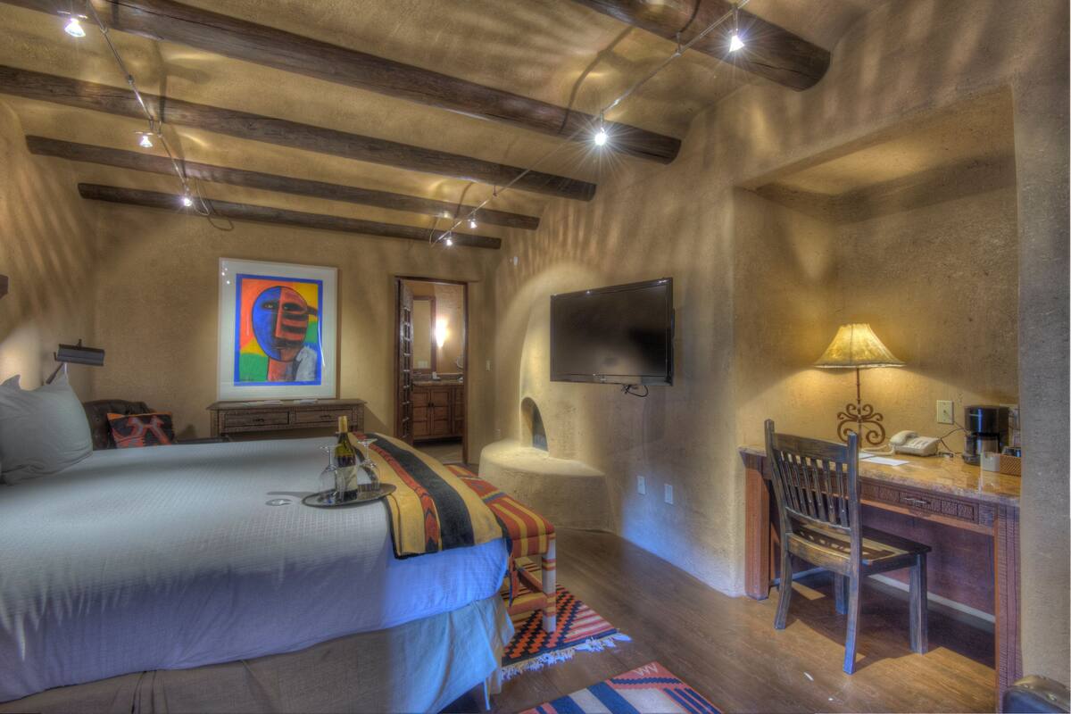 A bedroom with a bed, a desk, a chair, a television, and a painting on the wall.