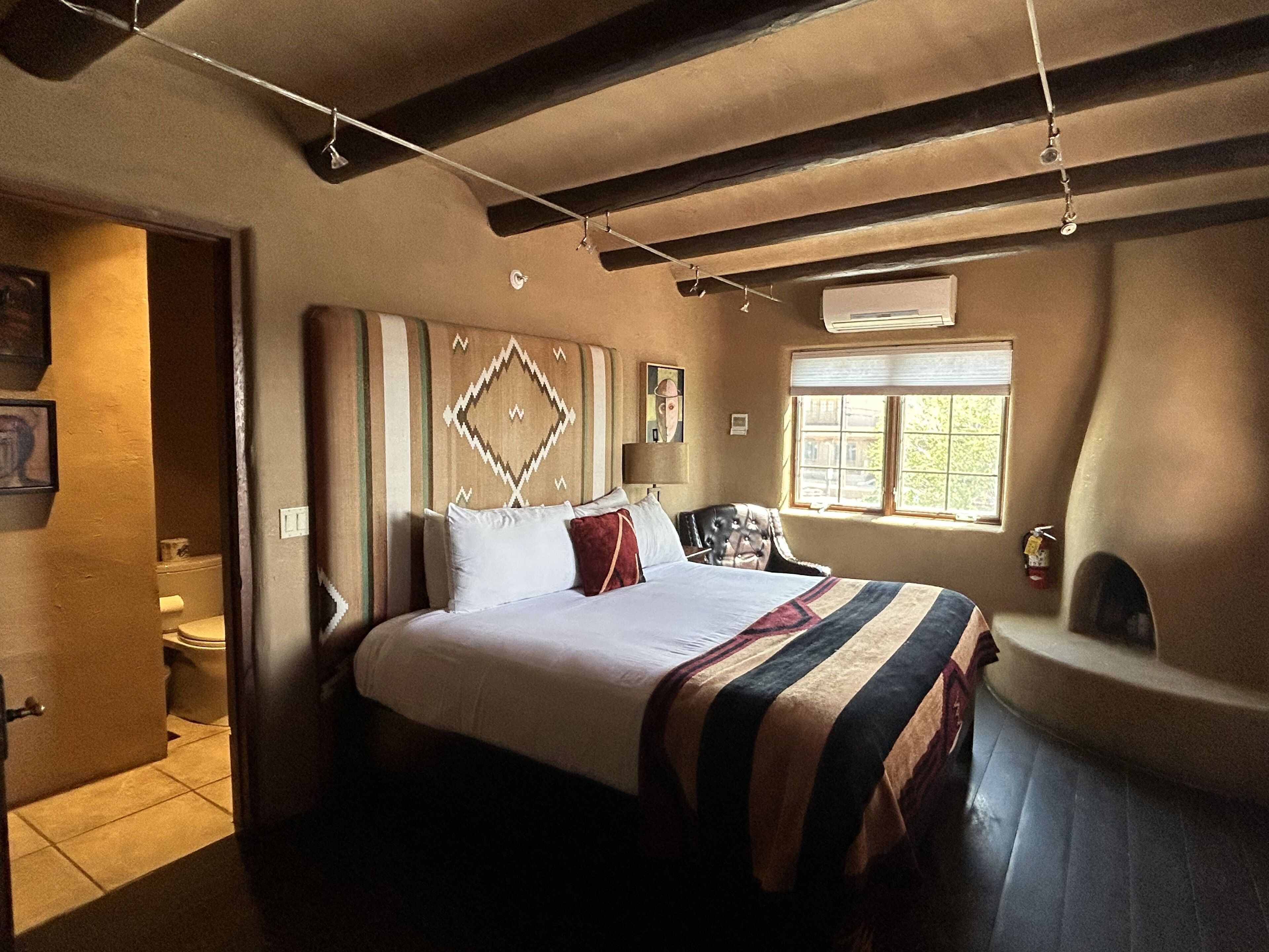 A bedroom with a bed, a chair, a window, and a bathroom.