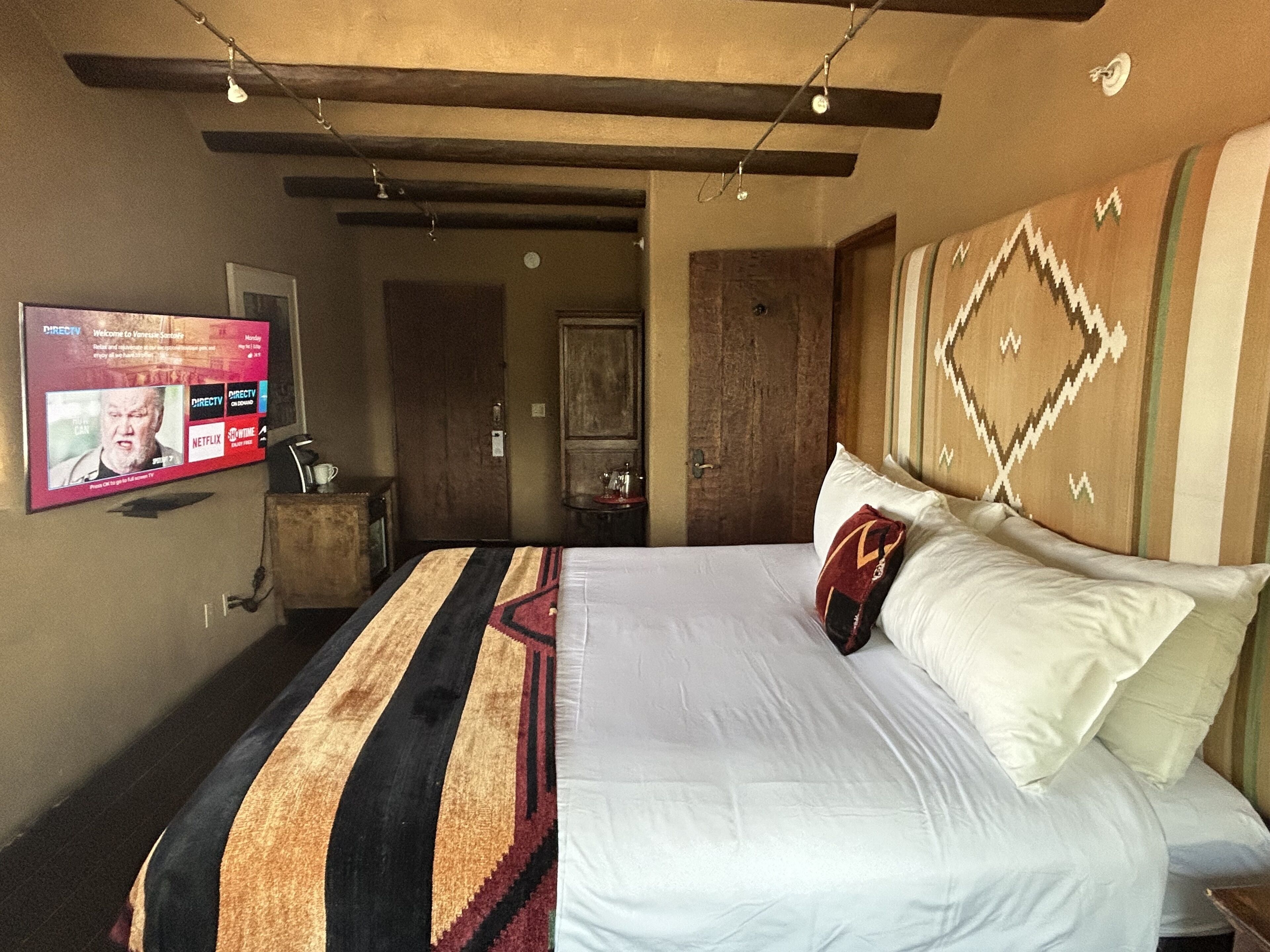Una habitación de hotel con cama, televisión montada en la pared y puerta que da a otra habitación.