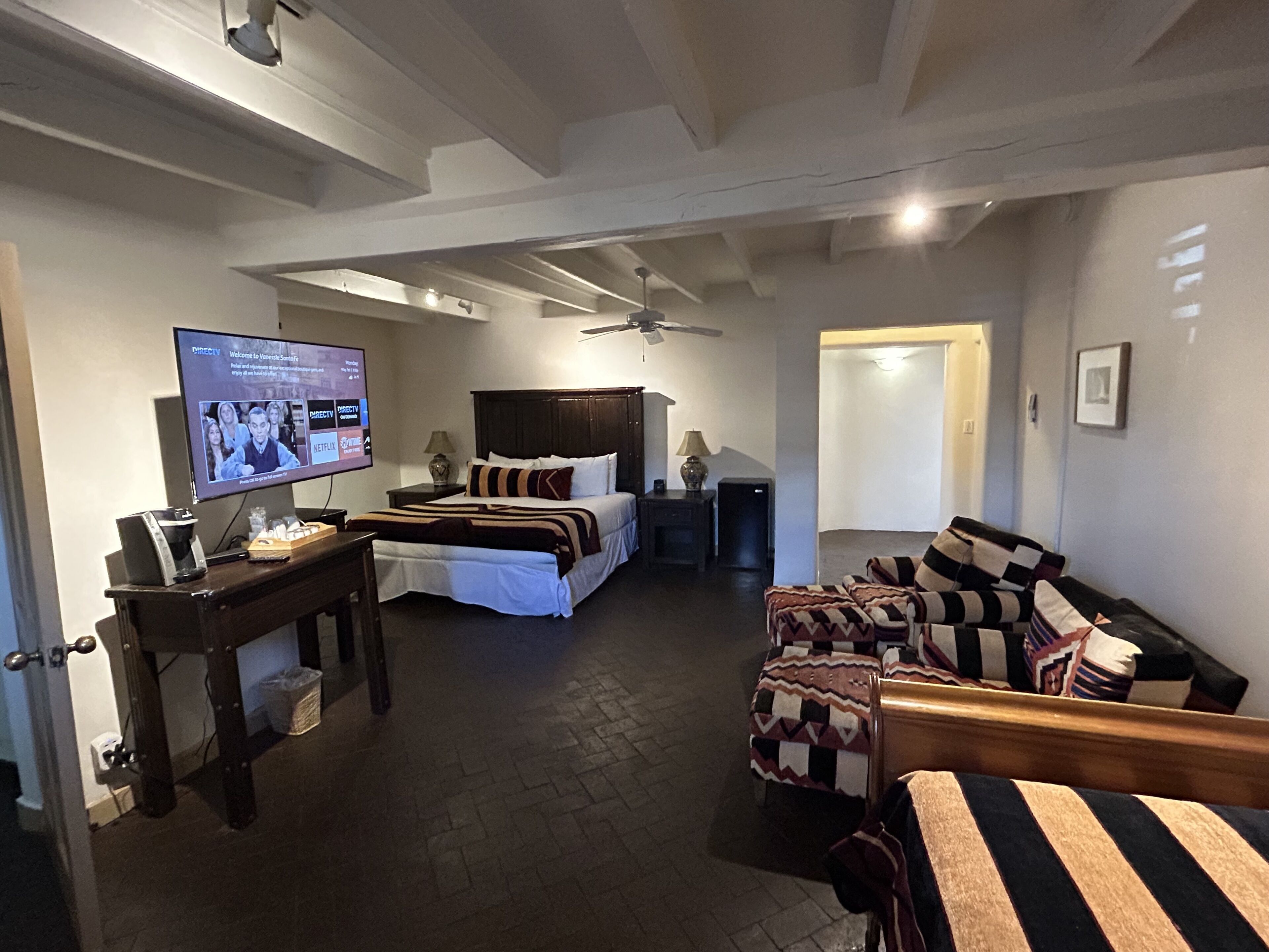 Una habitación de hotel con cama, sofá, televisor y ventilador de techo.