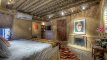 A bedroom with a bed, a fireplace, a TV, and a wooden ceiling.
