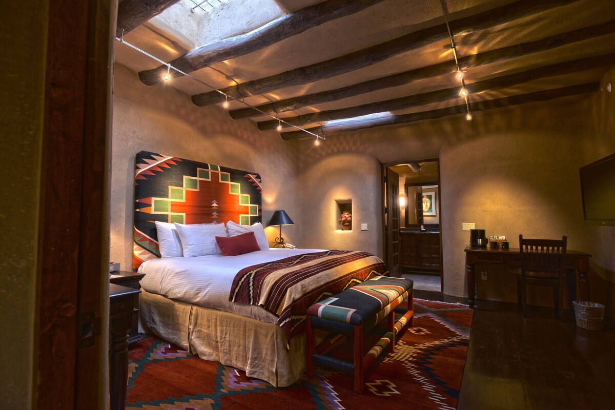A bedroom with a large bed, a bench, a desk, and a chair.