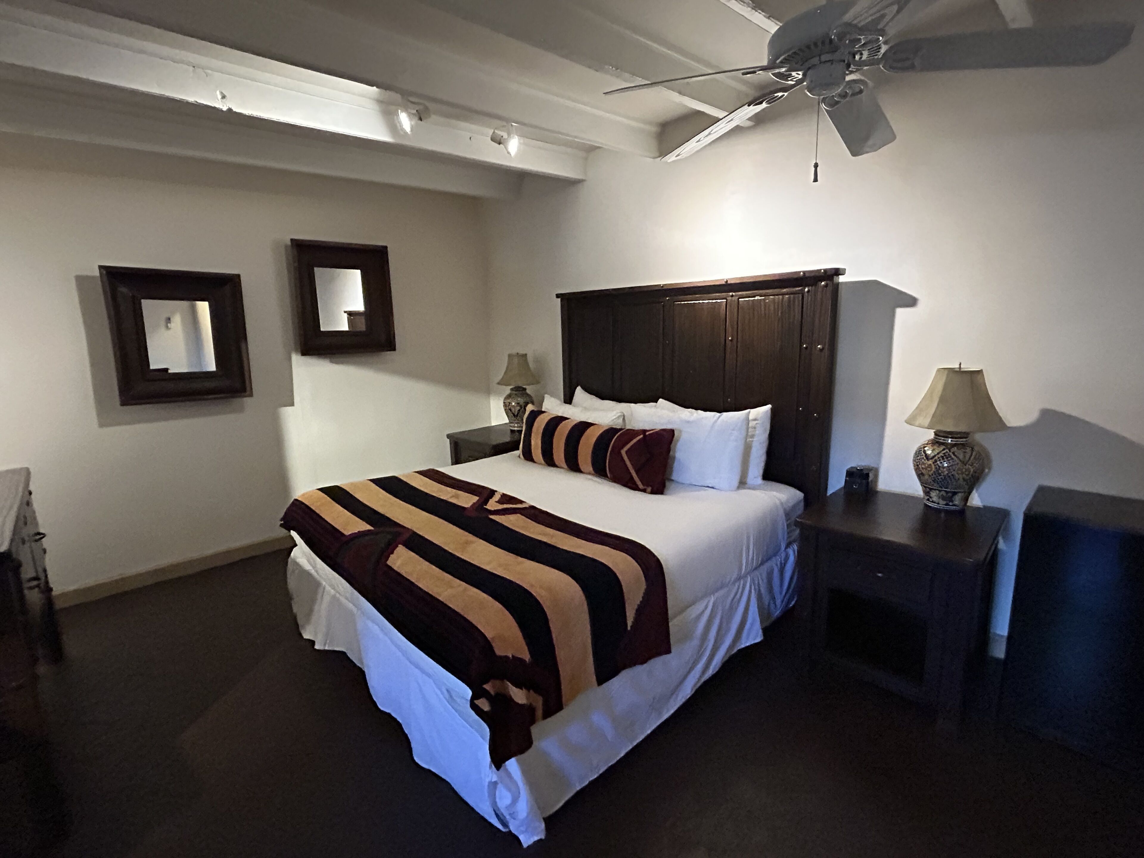 A hotel room with a bed, a nightstand, a lamp, a ceiling fan, and a mirror on the wall.
