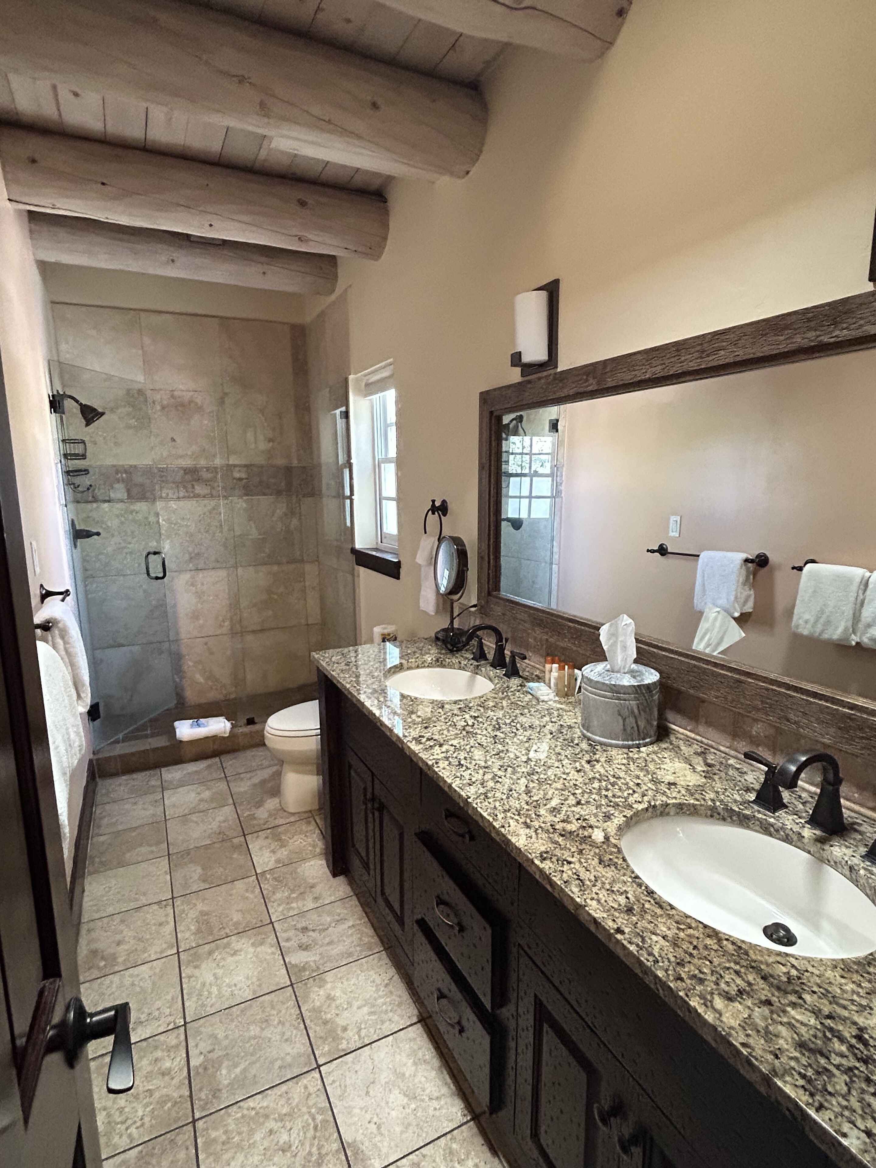 A bathroom with a granite countertop, two sinks, a large mirror, and a shower area.