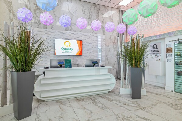 A hotel reception area with a marble wall, a digital display, and two potted plants. - Quality Inn and Conference Center Tampa-Brandon (Tampa)