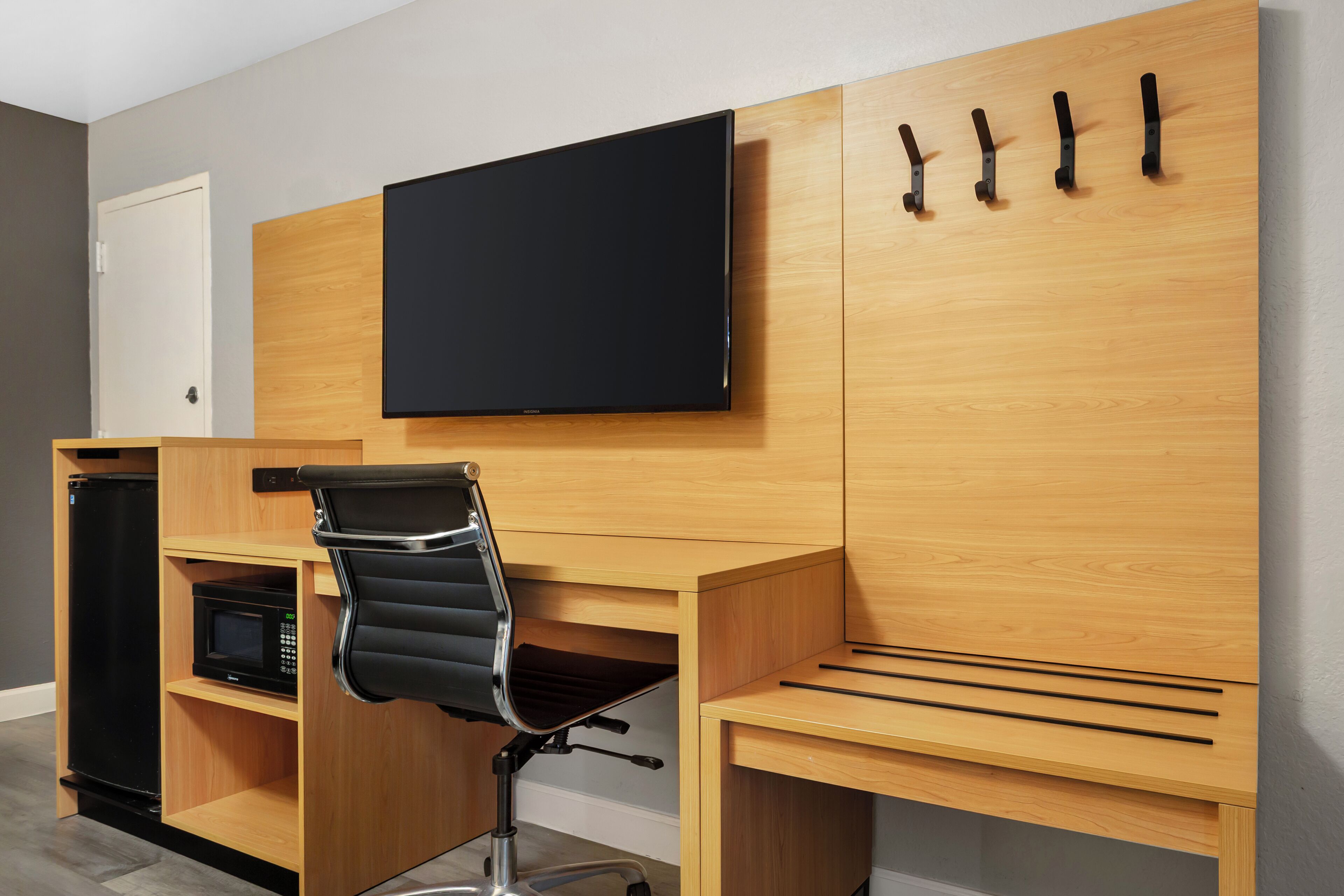 A modern office space with a wooden desk, a black office chair, a mounted flat-screen TV, and a microwave.