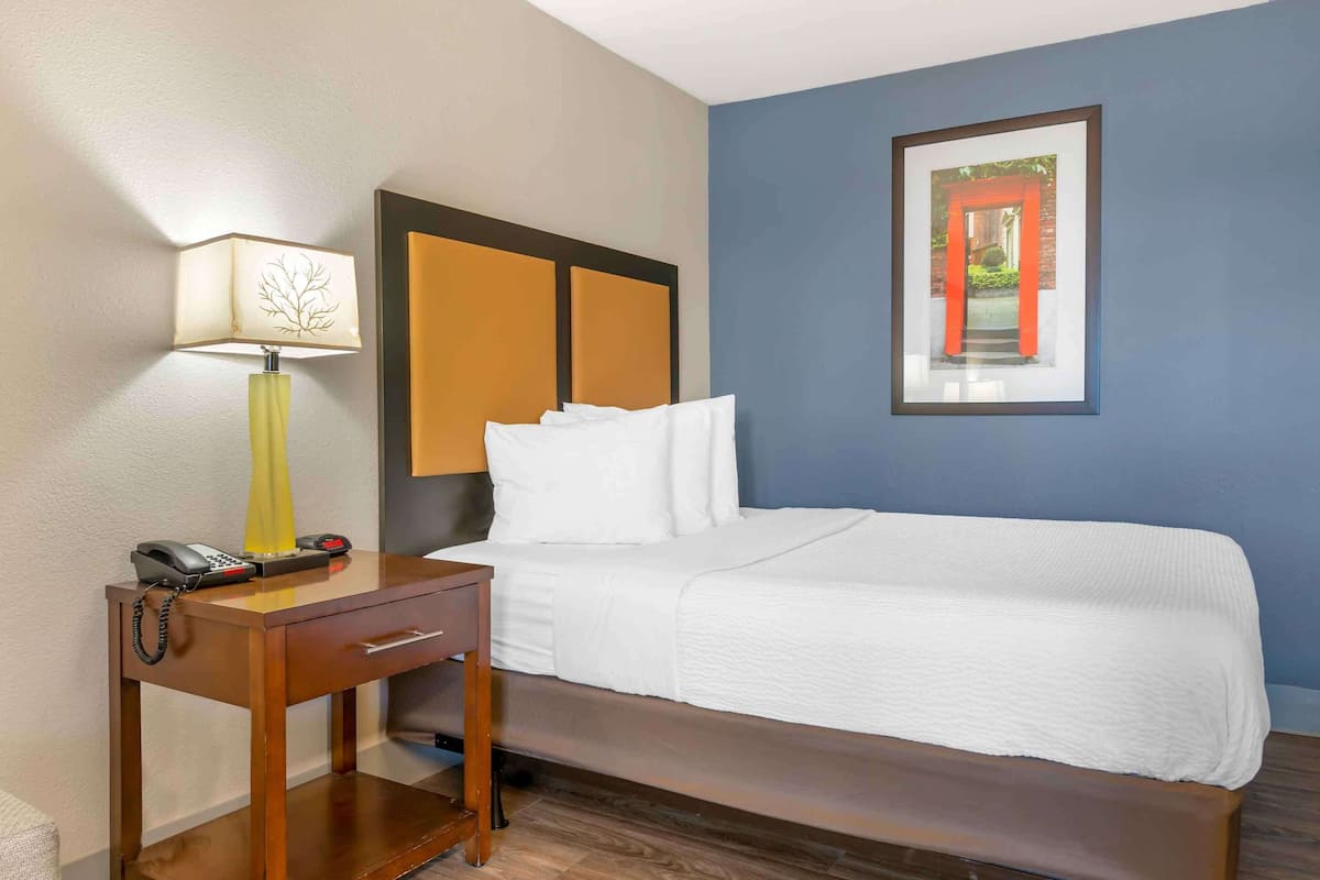 Una habitación de hotel con una cama, una mesita de noche con lámpara, un teléfono y un cuadro en la pared.