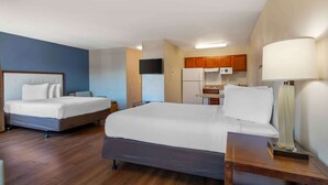 Una habitación de hotel con dos camas, kitchenette, un televisor de pantalla plana y una lámpara de noche.