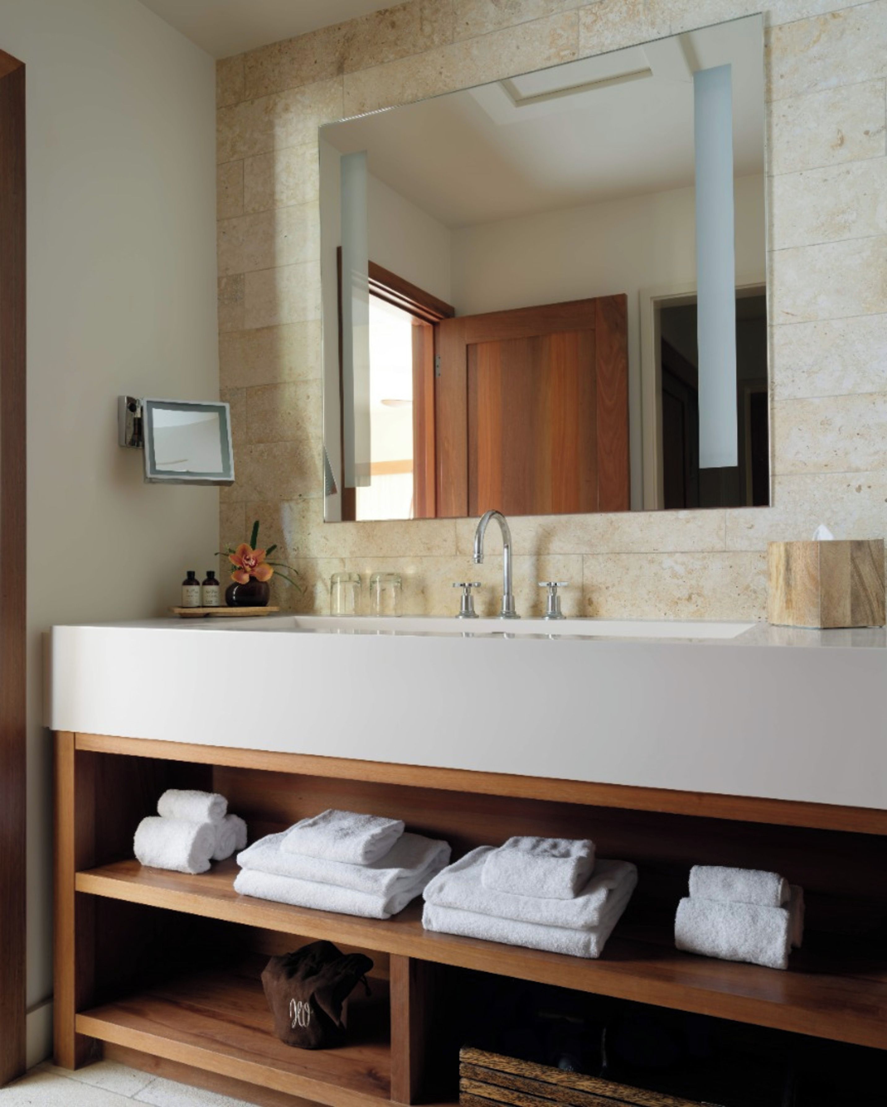 A bathroom with a large mirror, a white sink, and wooden shelves below.