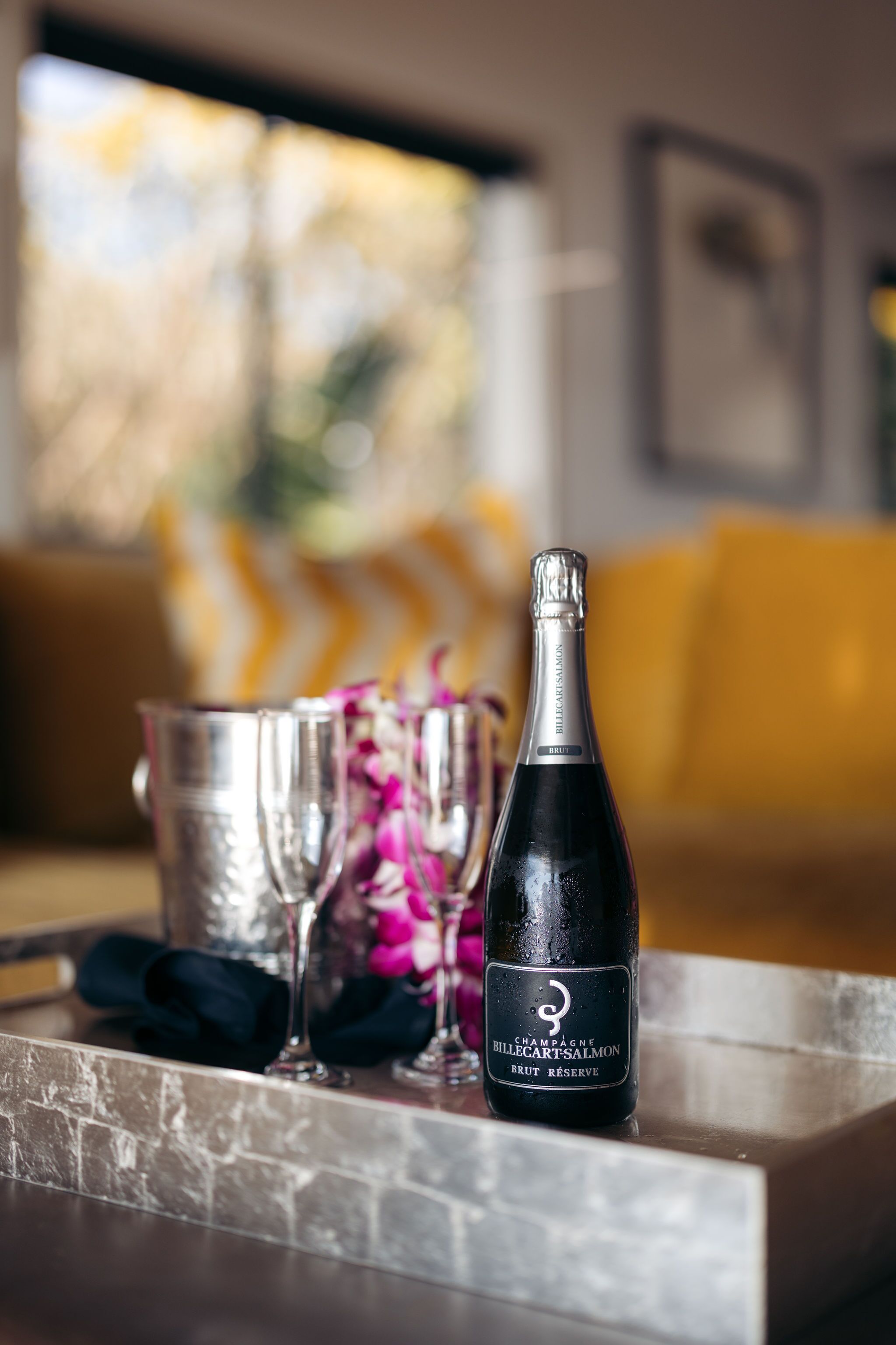 A bottle of champagne on a tray with two glasses and a flower arrangement.