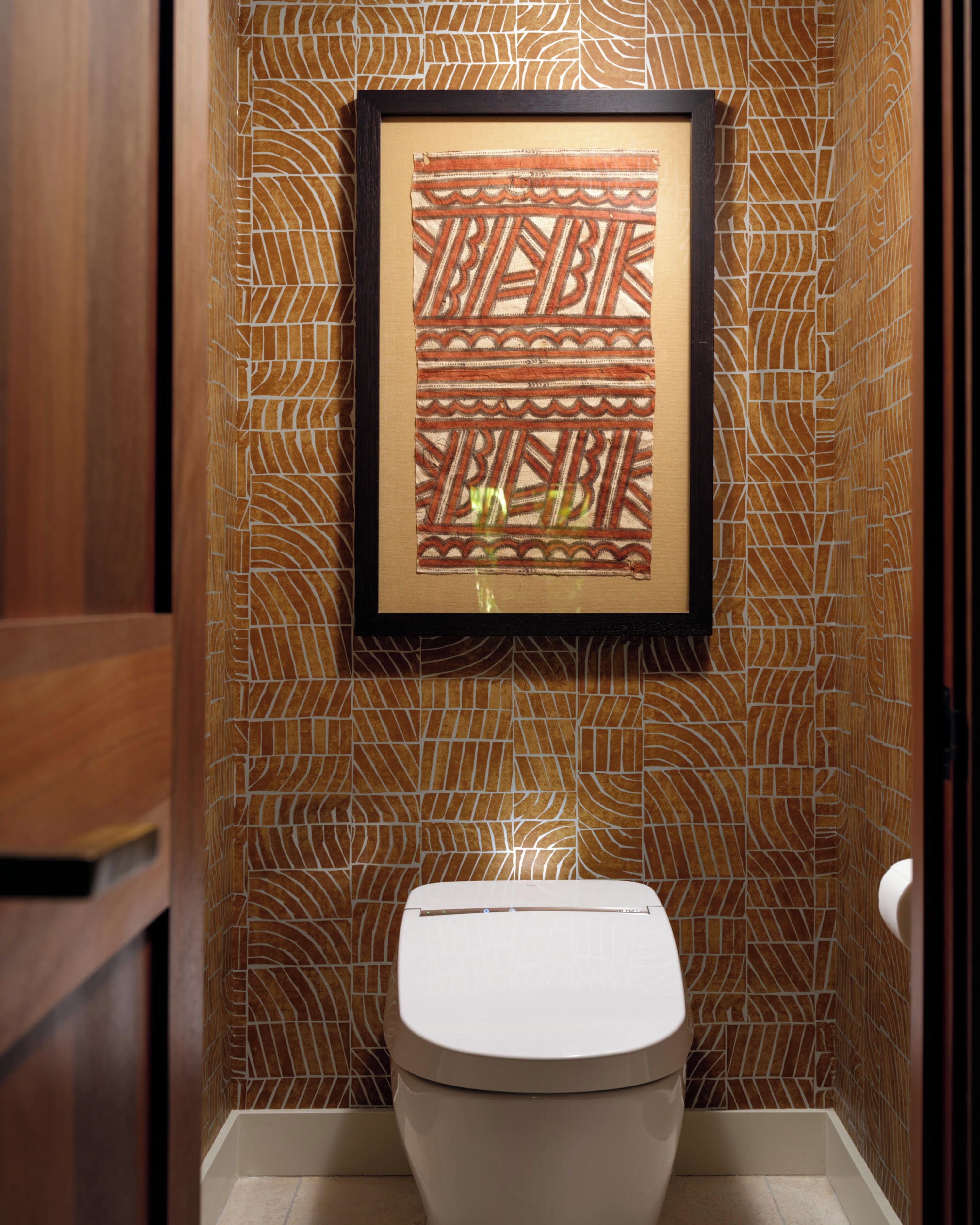 Une œuvre d’art encadrée, présentant un motif géométrique, est accrochée au mur au-dessus des toilettes dans une salle de bain.