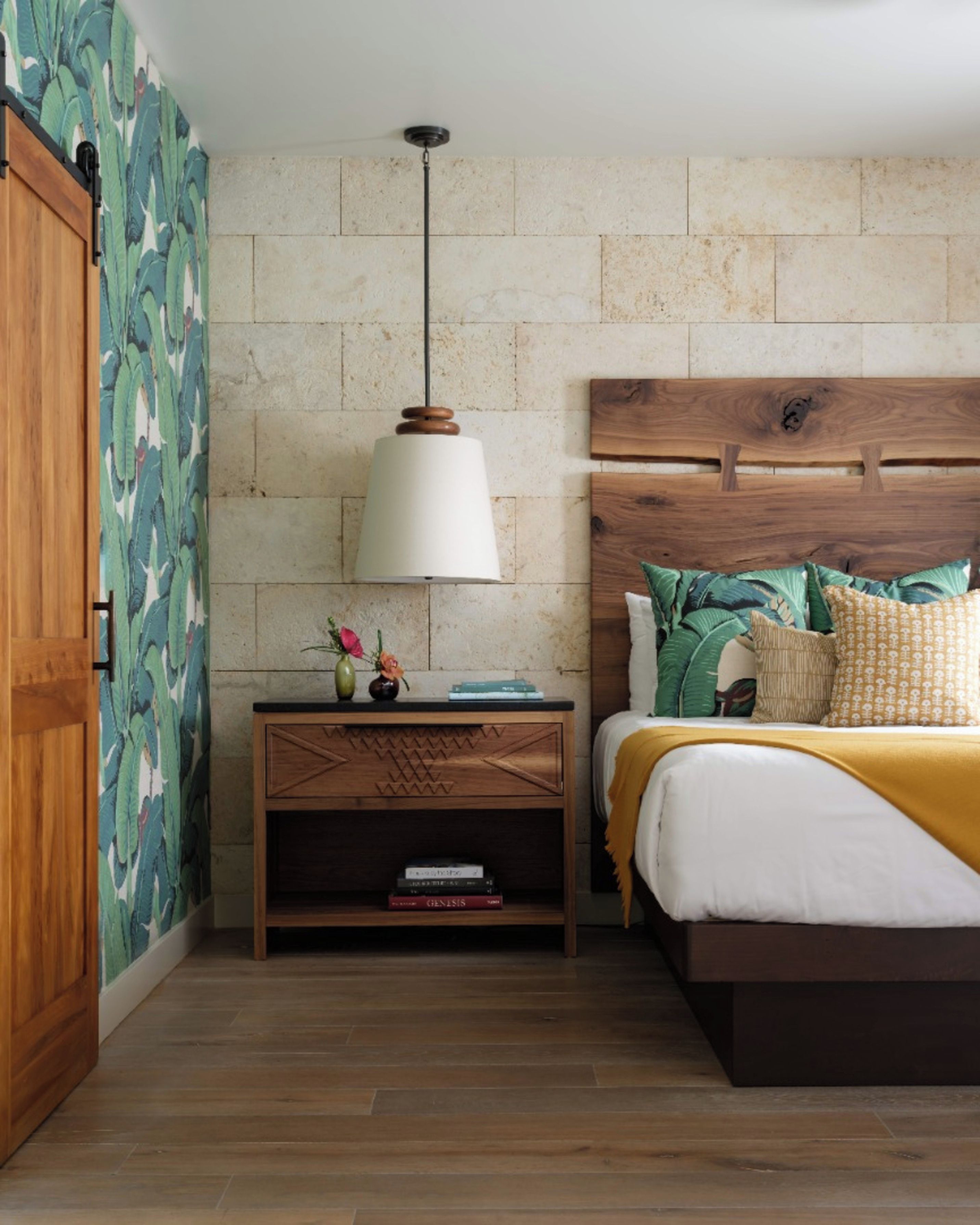 A bedroom with a wooden headboard, a bedside table with a lamp, and a bed with pillows and a blanket.