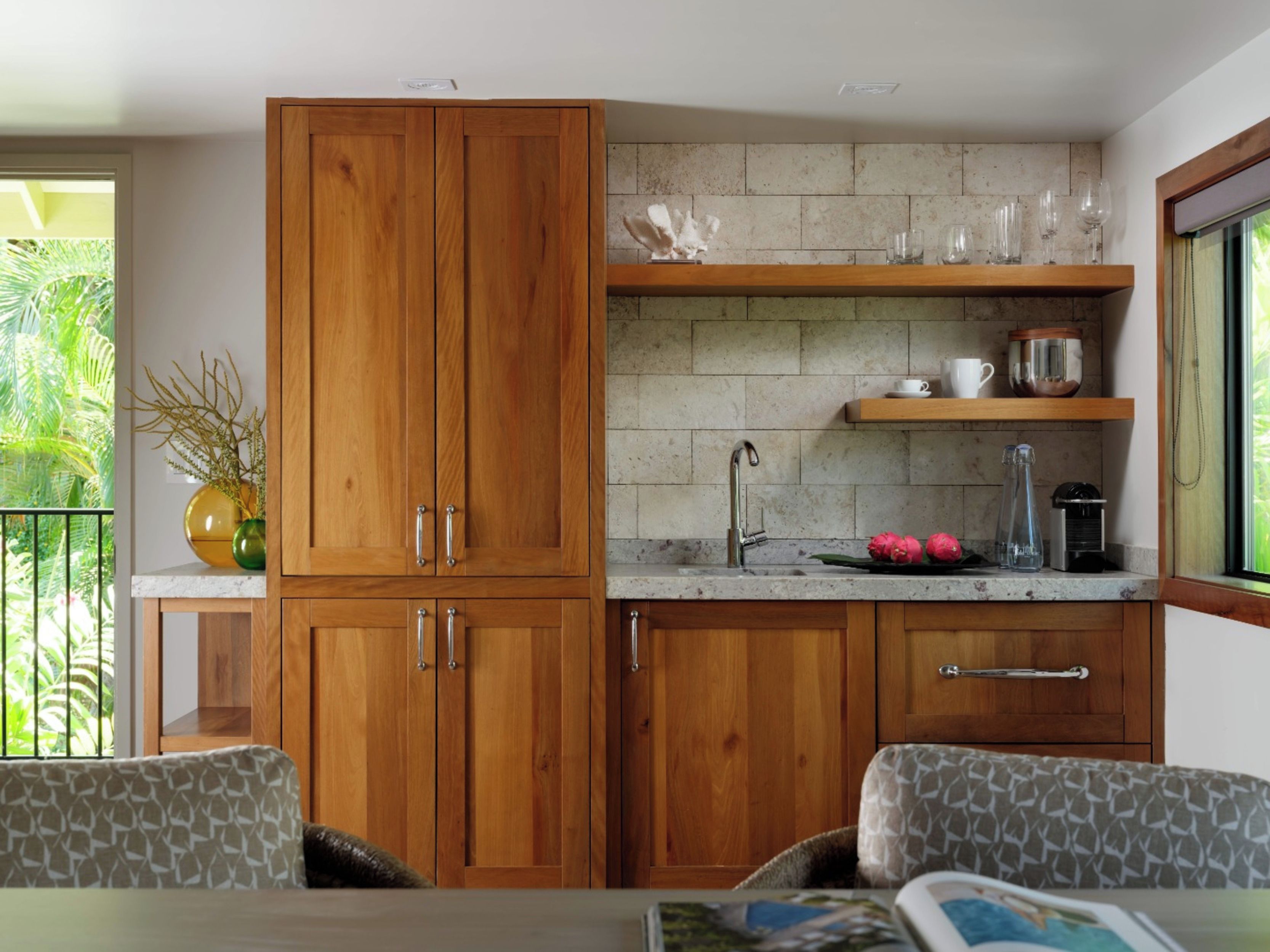 A kitchen with wooden cabinets, a marble countertop, and a window with a view of greenery.